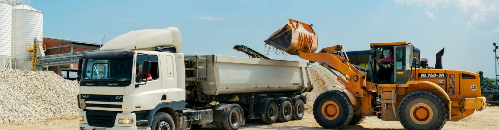 Excavator loading materials into a heavy-duty truck at a sunny construction site.